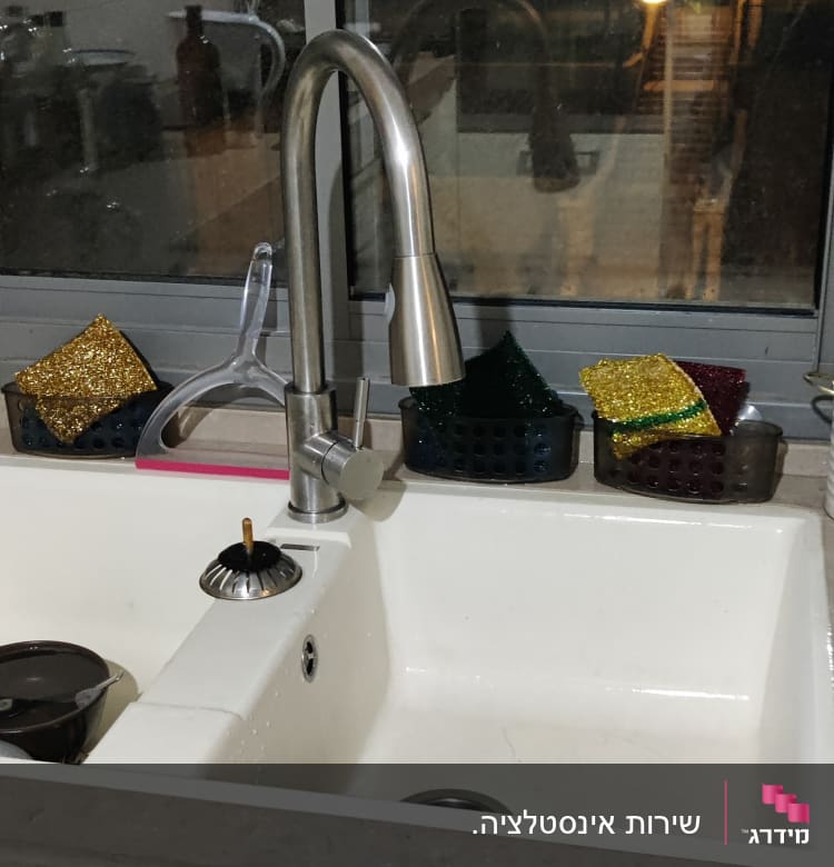 ברז נירוסטה מעל כיור מטבח עם ספוגים